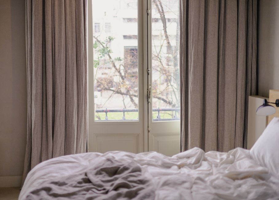 Daylight coming through a bedroom window beside parted linen curtains